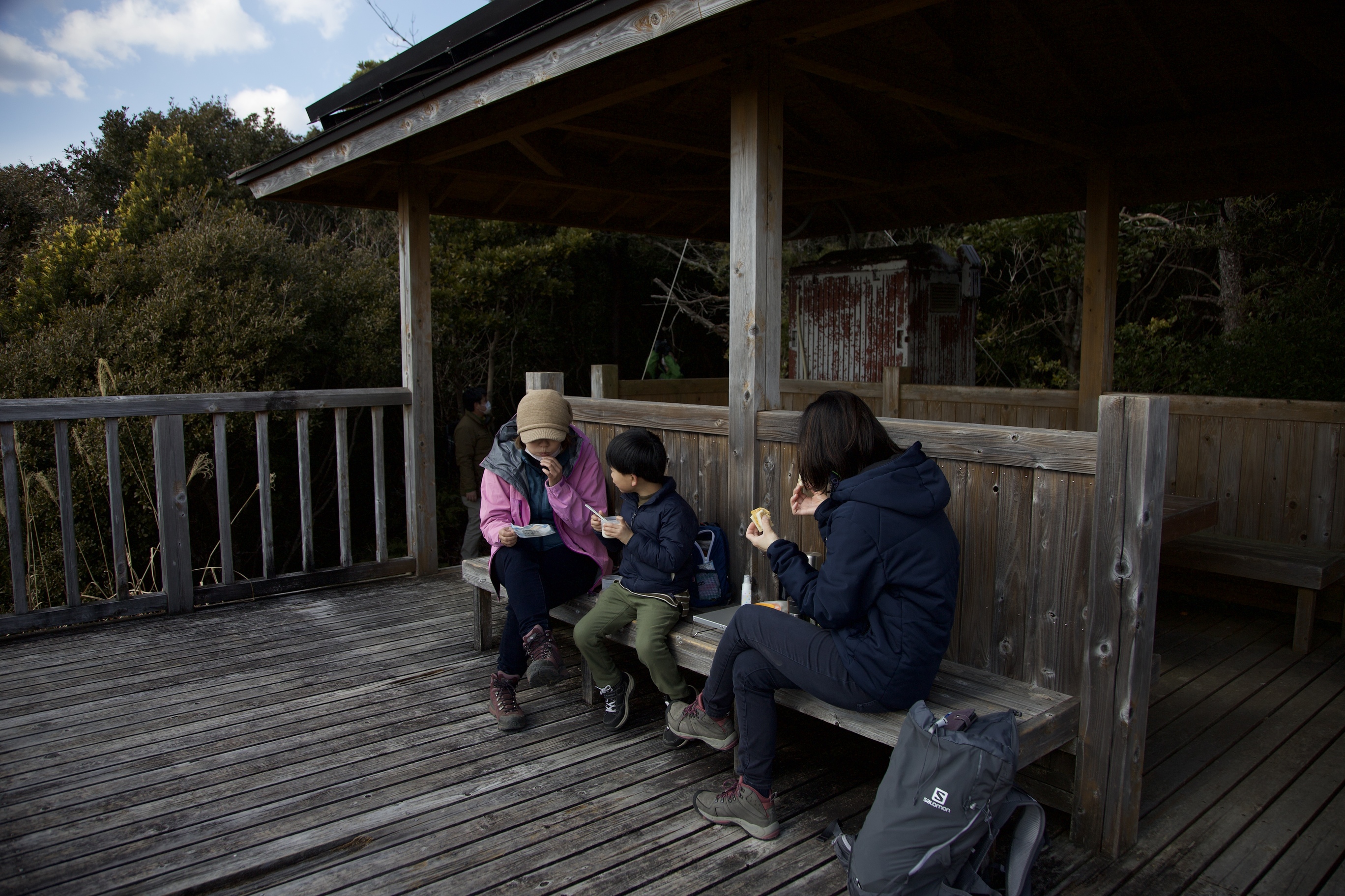 浅間山（せんげんさん）展望台で、家族連れが休憩している写真です。登山姿の大人2人と子ども1人が、東屋の外のベンチに座り、軽食をとっています。